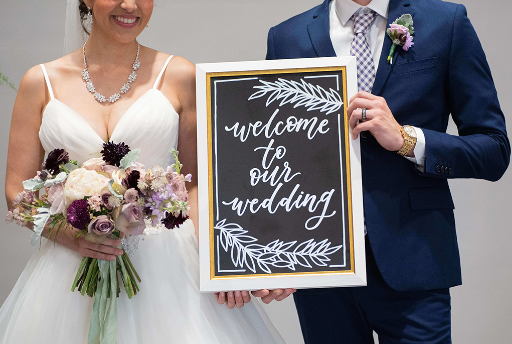 Married couple holding a sign that says Welcome to our Wedding