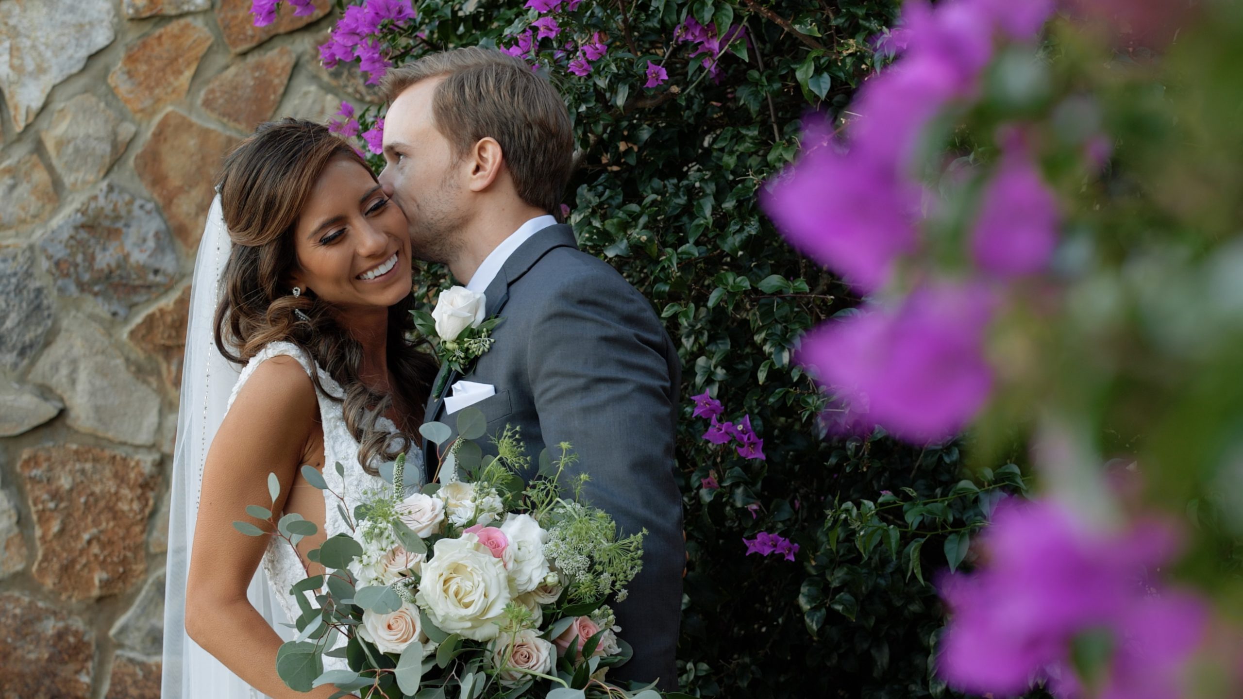 Married couple kissing by purple flowers at Bella Collina Wedding