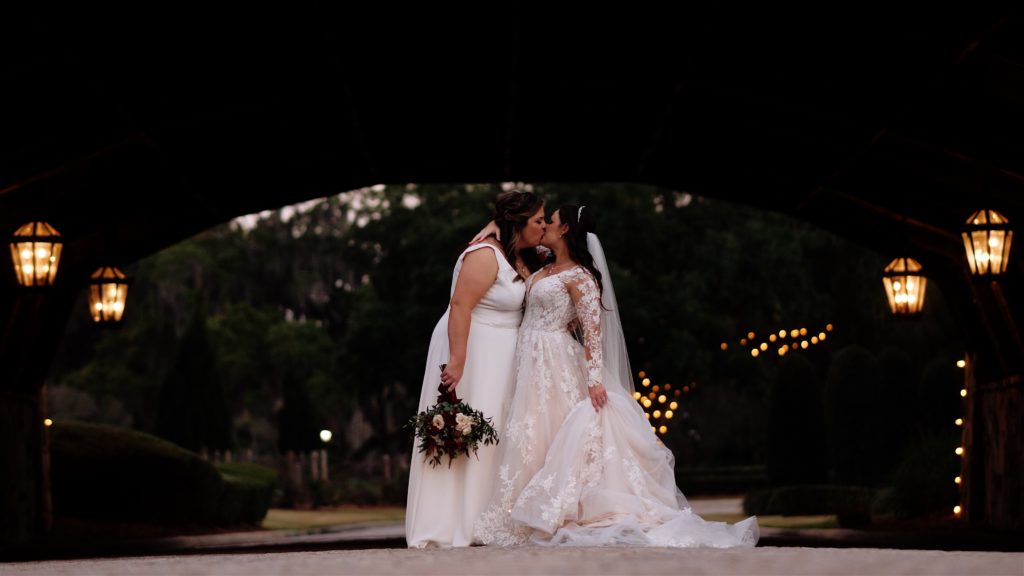 Two brides kissing under a bridge in the evening