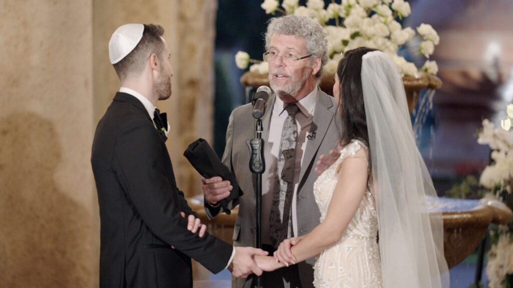 Rabbi holding glass to be broken at the end of the Jewish ceremony while looking at the groom